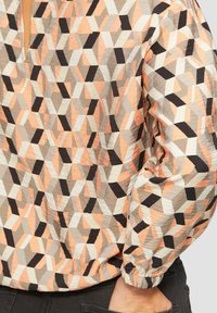 Patroon blouse met een geometrisch ontwerp in perzik, grijs en zwart. Heeft een elastische manchette en een stoffen textuur.