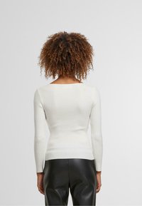 Bílý žebrovaný top s dlouhým rukávem a čtvercovým výstřihem, přiléhavý střih a texturovaná látka, spárovaný s černými koženými kalhotami.