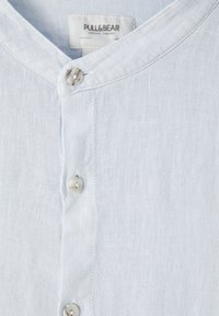 Jasnoniebieska lniana koszula z kołnierzem typu notch, z przodu zapinana na okrągłe guziki oraz subtelną teksturą tkaniny.