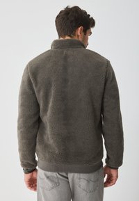 Fleece bunda v tmavě šedé barvě, texturovaná látka s vysokým límcem. Disponuje žebrovanými manžetami a spodním lemem, což zajišťuje měkký a útulný vzhled.