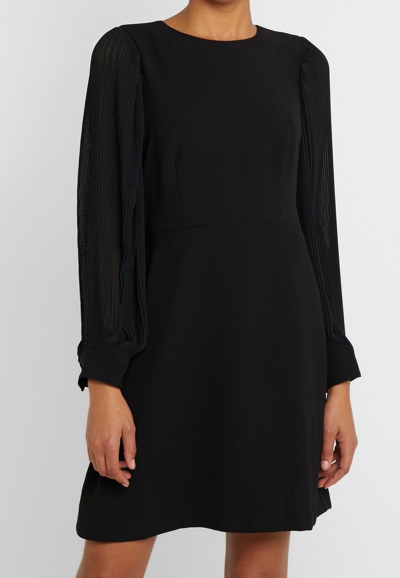 Schwarzes Kleid mit strukturiertem Oberteil und langen, gefältelten transparenten Ärmeln. Das Design hat einen runden Halsausschnitt und reicht bis über das Knie.