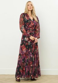 Lång, genomskinlig blommig klänning med röda och lila nyanser på en svart bakgrund, med ett insnärjt midja och lager på lager kjol. Långa ärmar, V-hals.