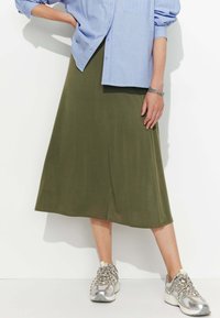 Jupe olive, longueur genou, en tissu lisse, associée à une chemise boutonnée bleu clair et des baskets métalliques avec un design texturé.