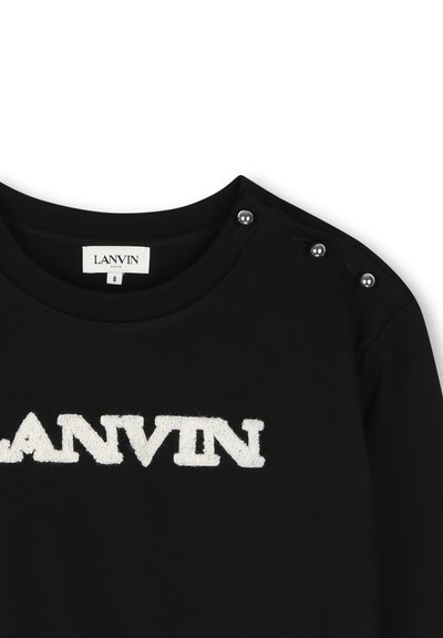 Μαύρο πουκάμισο Lanvin με λευκό υφασμάτινο λογότυπο στο στήθος και τρία ασημένια κουμπιά στον δεξί ώμο κοντά στη στρογγυλή λαιμόκοψη.