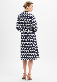 Navy und weiße gemusterte Kleid mit einem ausgestellten Design, langen Ärmeln und tailliertem Schnitt. Besitzt einen klassischen Kragen und eine Knopfverschluss.