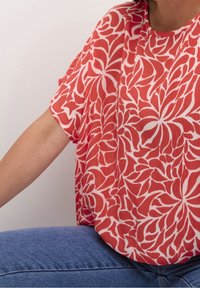 Top de manga corta rojo y blanco con un patrón floral, fabricado en tejido ligero, con cuello redondo y corte holgado.