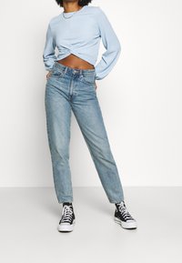 Ljust blå, texturerad långärmad topp knuten vid fållen, ihopparad med högmidjade, ljusblå jeans och svarta låga sneakers.