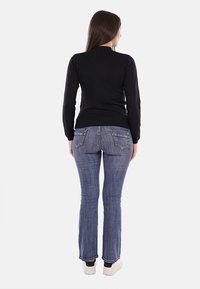 Maglietta nera a maniche lunghe con un design aderente, abbinata a jeans svasati di un blu chiaro. L'outfit è completato da sneakers bianche.