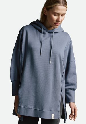 Lange blaue Kapuzenjacke aus weichem Stoff, mit einer Kordelzugkapuze, seitlichen Schlitzen und einem kleinen Logosticker am Saum.