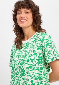 Groen bloemenpatroon t-shirt op een witte achtergrond, gemaakt van zachte stof, met korte mouwen en een ronde halslijn.