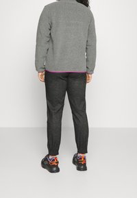 Harmaa fleecetakki, jossa on purppuranvärinen helma, yhdistetty tummanharmaisiin kapeneviin housuihin ja mustiin tennareihin, joissa on oransseja ja purppuranvärisiä yksityiskohtia.