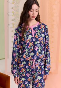 Tumesinise värviga lilleline pidžaamakomplekt roosade detailidega, millel on pikad varrukad, nööbitav kaelus, kummiga vöökoht ning värvikad lille- ja jänesemustrid.