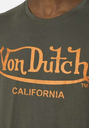 Primer plano de una camiseta verde con texto naranja desvanecido que dice "Von Dutch" y "CALIFORNIA" en el pecho.