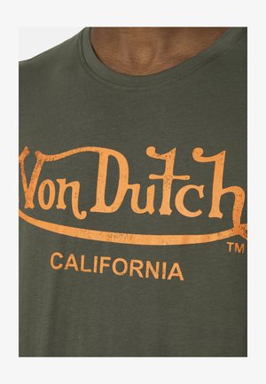 Primer plano de una camiseta verde con texto naranja desvanecido que dice "Von Dutch" y "CALIFORNIA" en el pecho.