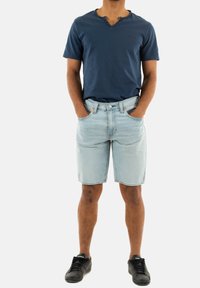 Camisa de manga corta azul marino con escote en V, pantalones cortos de mezclilla azul claro con bolsillos y zapatillas negras. Material de algodón, diseño casual.