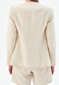 Kremowa marynarka z tweedu w poziome paski. Długie rękawy, wyraźna sylwetka i teksturowany materiał. W zestawie z dopasowanymi szortami.