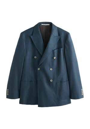 Man wearing a navy blue double-breasted suit, white button-down shirt, and patterned brown tie against a neutral background.