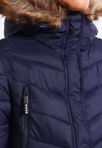 Marinblå dunjacka med avtagbar, pälsfodrad huva, quiltad design och bröstficka med dragkedja. Mjuk textur och isolerande material.