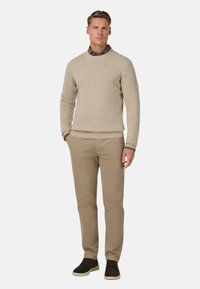 Suéter de punto texturizado en color beige claro con cuello redondo, acompañado de pantalones marrón claro y zapatillas de ante oscuras. Diseño simple y elegante.