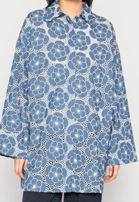 Camisa de estampado floral azul con un corte relajado, que presenta un cierre de botones en el frente, un gran cuello y mangas de campana, confeccionada con tejido estampado.