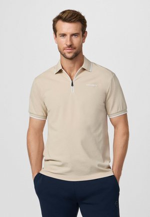 Polo beige con cuello de cremallera y sutiles detalles blancos. Corte ajustado, mangas cortas y detalle de logotipo bordado en el pecho.
