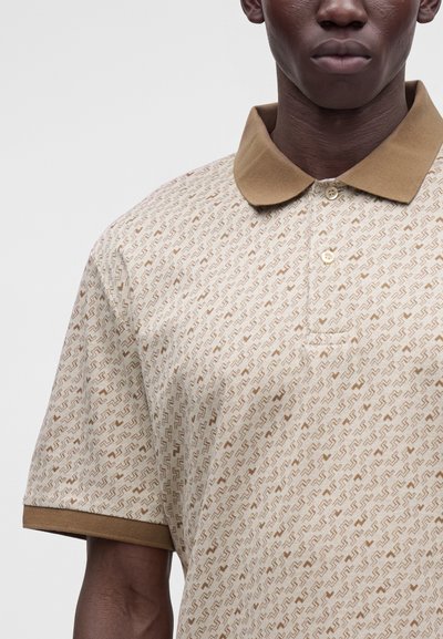 Gros plan d'une personne portant un polo beige à motif avec un col et des poignets marron, deux boutons fermés au niveau du cou.