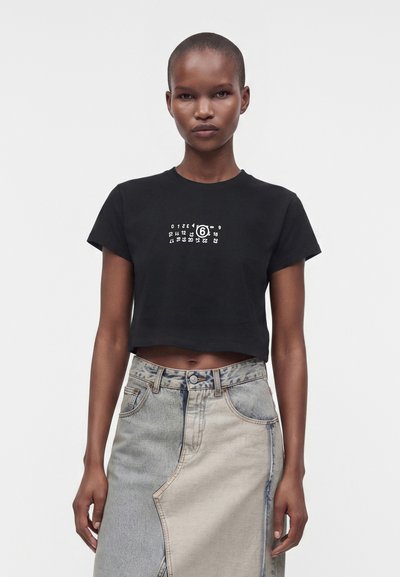 Young woman with short hair wearing black cropped T-shirt with white number print and two-tone denim skirt with front seam.