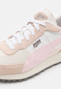 Sneaker aus einer Mischung von Wildleder und Stoffmaterialien, überwiegend weiß mit hellrosa Akzenten und geprägtem Logo an der Seite.