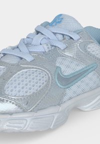 Ανοιχτό μπλε και γκρι αθλητικό παπούτσι Nike με ύφασμα δίχτυ και υφή φιδιού, κεντημένο λογότυπο Swoosh και παχιά σόλα σε λευκό φόντο.