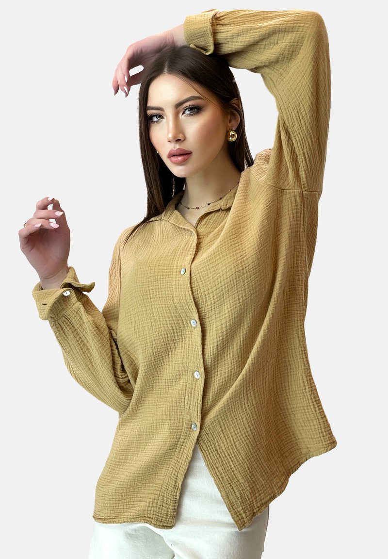 Camicia a maniche lunghe con bottoni in tessuto marrone chiaro, texturizzato e con finitura stropicciata; presenta orlo arrotondato e polsini con bottone.
