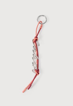 Porte-clés en fil d'argent formant le mot « enjoy », attaché à un anneau avec deux cordons noués rouges et corail sur un fond blanc.