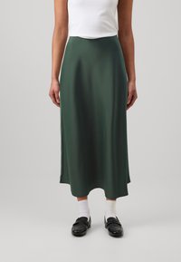 Fustă midi din satin verde, cu o textură netedă, formă fluidă și talie elastică, asortată cu mocasini negri și șosete albe.
