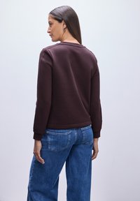 Felpa marrone realizzata in un tessuto morbido, con scollo rotondo, polsini a coste e una vestibilità comoda, abbinata a jeans a gamba larga di colore azzurro chiaro.