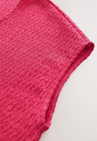 Section d'un vêtement rose texturé avec un design en tissu froissé. Des bords lisses et un col arrondi sont visibles, mettant en valeur le drapé du matériau.