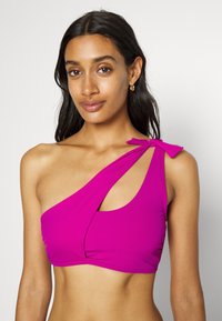 Top bikini fucsia a spalla unica con design intrecciato, taglio laterale e un dettaglio a fiocco sulla spalla. Tessuto liscio e elasticizzato.