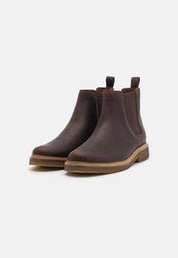 Bottes Chelsea en cuir marron à finition lisse, avec inserts élastiques sur les côtés, bout arrondi et semelle solide et texturée. Dotées de languettes de traction en haut.