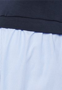 Blue and white striped skirt with gathered texture, paired with a dark blue fitted top. Soft, lightweight fabric with subtle sheen.