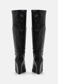Bottes en cuir noir montant jusqu'au genou, à texture lisse, talons carrés et coupe ajustée, présentant des coutures minimales et sans pièces métalliques apparentes.