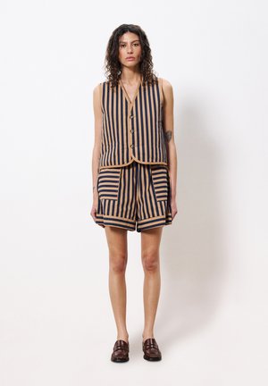 Ensemble de gilet rayé et de shorts en marine et beige, comprenant un gilet boutonné, des poches avant et des fentes sur les côtés. Porté avec des chaussures marron foncé.