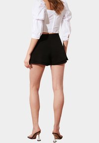 Černé šortky s vysokým pasem a rozšířeným lemem, doplněné těsným bílým krátkým topem s nafouknutými rukávy a zipem na zádech.