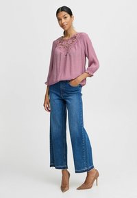 Lys mauve bluse med blonder, lange ærmer og flæseærmer, kombineret med høj talje, brede blå denim jeans og nude hæle.