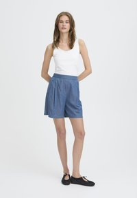 Denim šortai su raukšlėmis ir elastinga juosta, derinami su balta marškinėlių palaidine ir juodais baleto bateliais. Švelni medžiaga, kasdieniškas dizainas.