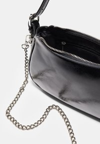 Borsa a mano in pelle nera con forma arrotondata, zip silver e tracolla a catena silver removibile. Interno con una tasca con zip.