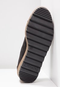 Semelle de chaussure en daim noir avec une finition en caoutchouc texturé, présentant des rainures horizontales et un logo de marque. Taille estampillée 37.