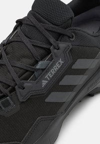 Schwarze Terrex-Schuhe mit einem strukturierten Obermaterial aus Stoff, grauen Akzenten, einem sicheren Schnürsystem und einer Gummi-Außensohle mit einem robusten Profil.