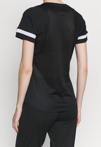 Svart atletisk t-shirt med meshnät på ryggen, korta ärmar med vita ränder och en figurnära passform. Mjukt, lätt tyg med en slät yta.