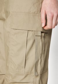 Beiga cargobyxor i bomullsblandning, med en sidoficka med klaff, vertikala veck och en vävd remaccent.