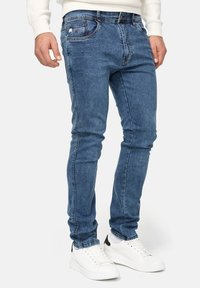 Jeans en denim bleu slim fit avec une légère élasticité, présentant un design classique à cinq poches, un léger délavage et des coutures contrastées.