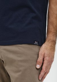 Marineblå bomulds T-shirt med korte ærmer, side søm mærke der læser "FQ1924 ORIGINAL," parret med lysebeige bukser.