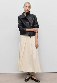 Black leather cropped jacket, cream pleated skirt, black flats with studded ankle straps. Smooth texture, structured design, contrasting colors.